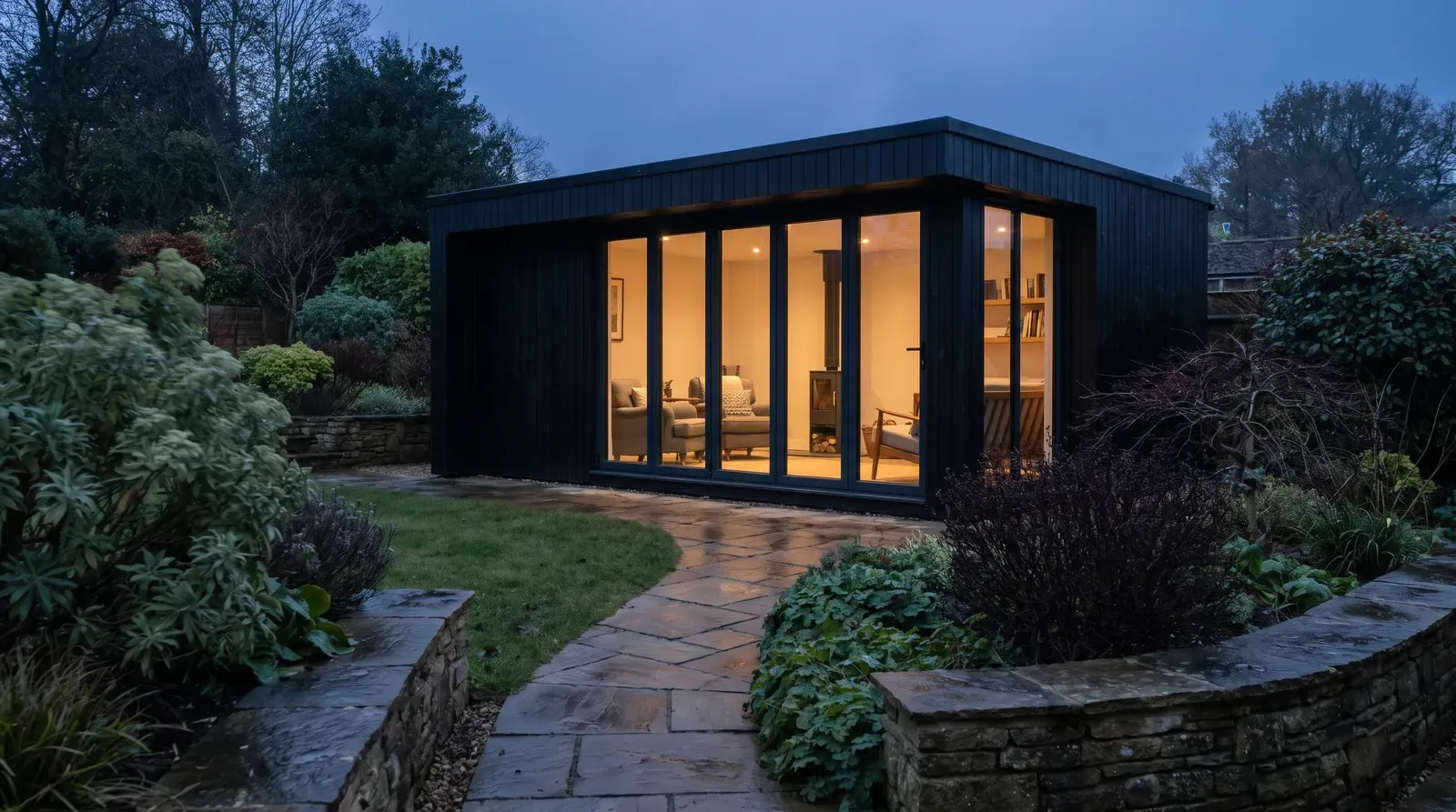 Modern glazed garden room glowing at dusk at the end of a landscaped British garden